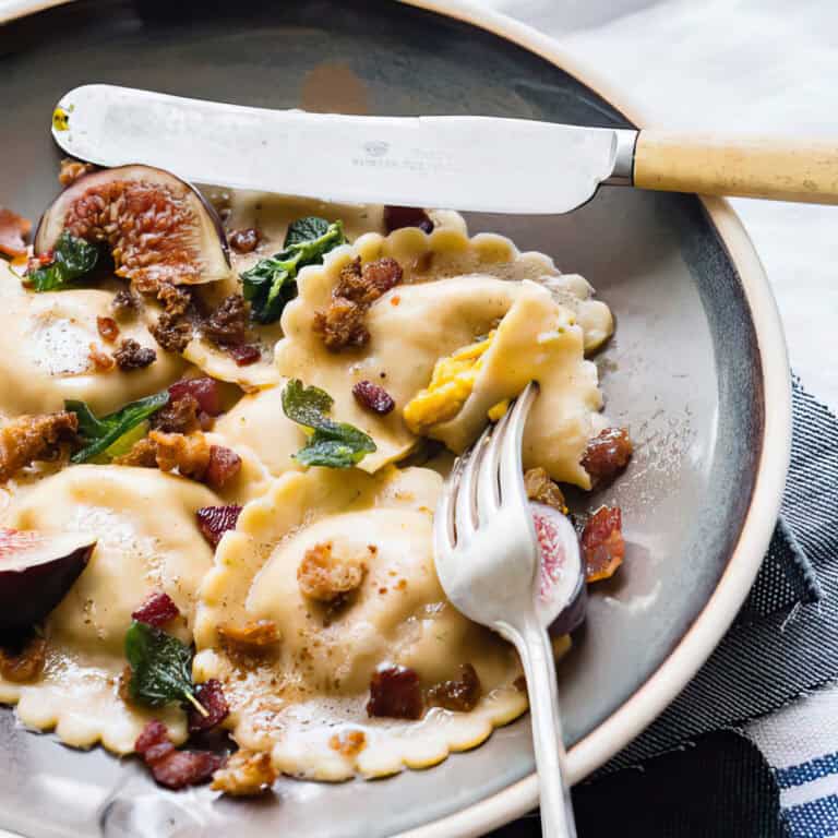 Pumpkin ravioli with sage and brown butter on a white table.