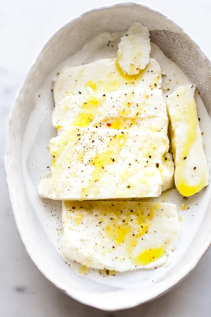 Sliced halloumi in a dish with oil and salt and pepper.