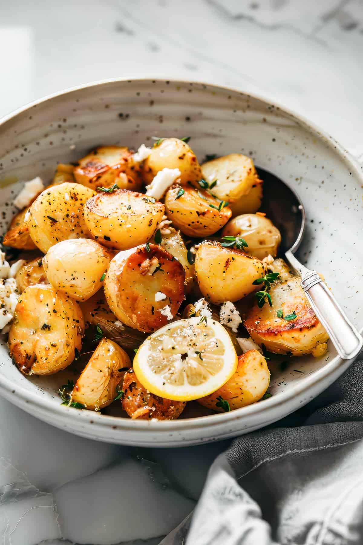 Greek roast potatoes with lemon and feta in a white bowl.