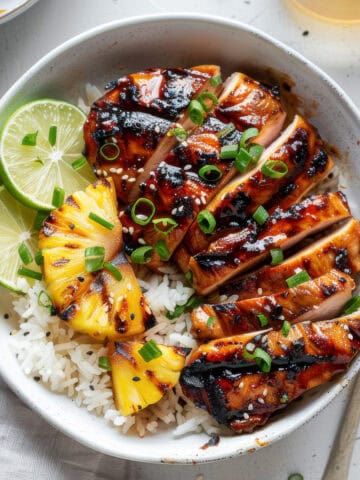 Grilled Asian chicken over rice in a bowl with limes.