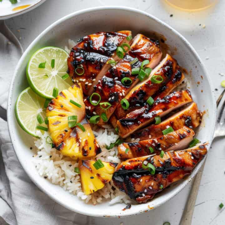 Grilled Asian chicken over rice in a bowl with limes.