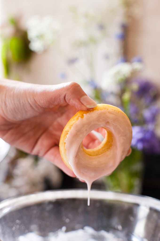 Baked donuts being dipped in glaze.