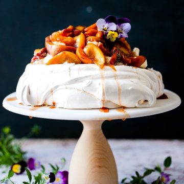 Roasted peach pavlova with flowers on a cake stand.