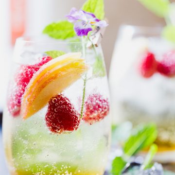 Peach sangria in a glass with raspberries.