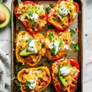 Chicken fajita stuffed peppers with sour cream, cheese and avocado on a baking tray.