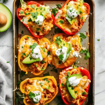 Chicken fajita stuffed peppers with sour cream, cheese and avocado on a baking tray.