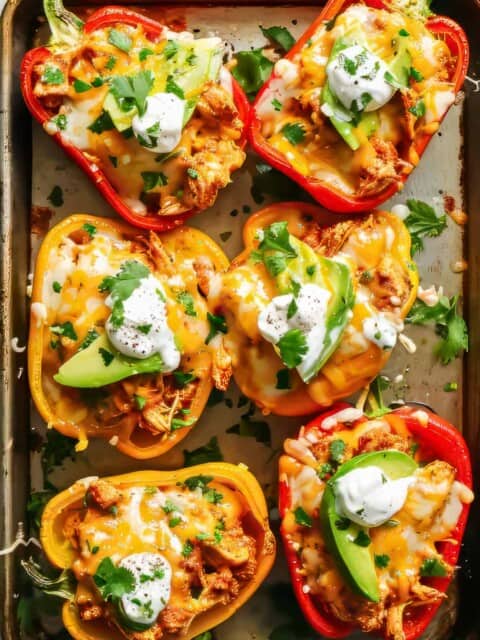 Chicken fajita stuffed peppers with sour cream, cheese and avocado on a baking tray.