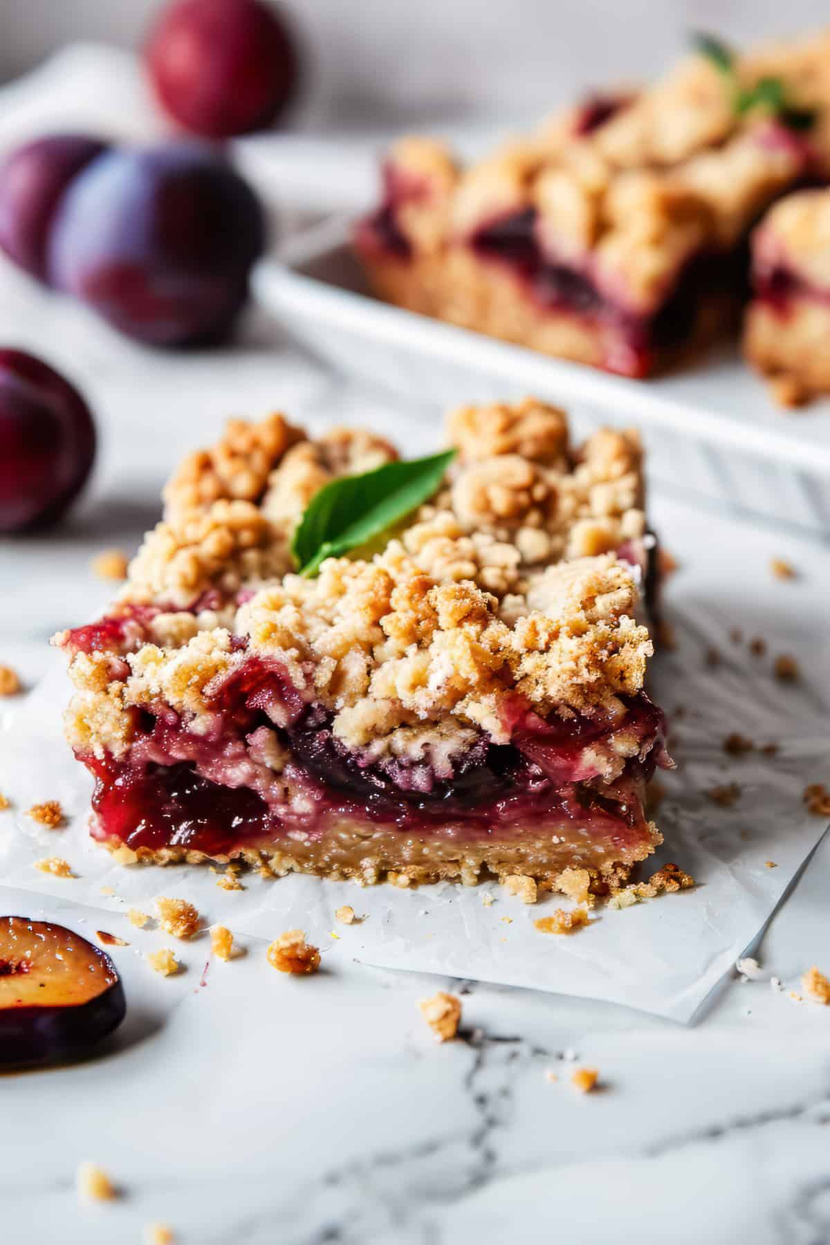 Plum bars with oat crumble topping on a piece of baking paper.