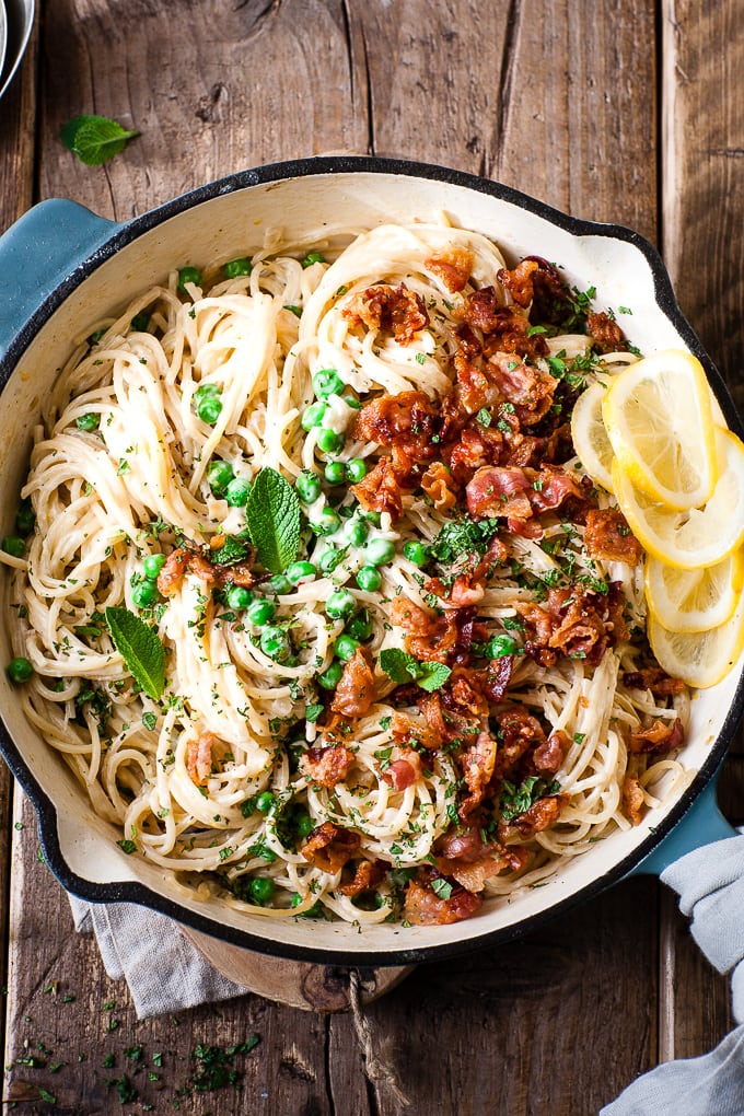 Creamy one pot pasta with bacon and peas in a skillet on a wooden table.