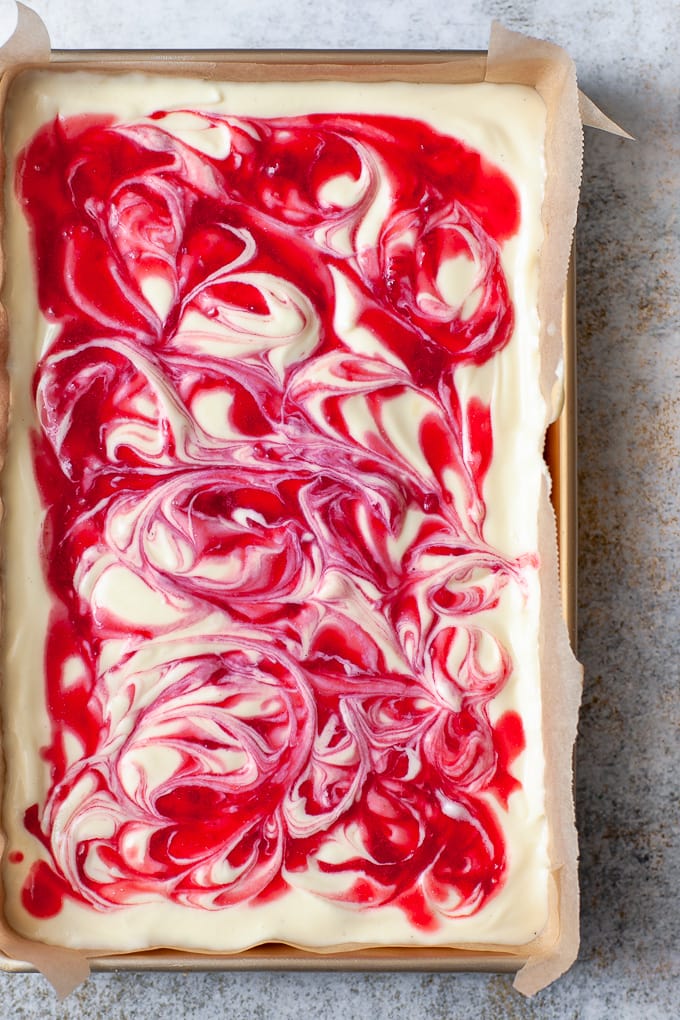 Swirls of raspberry sauce in cheesecake bars.