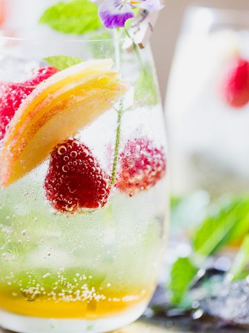 Peach sangria in a glass with raspberries.