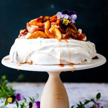 Pavlova with roasted fruit on a cake stand.