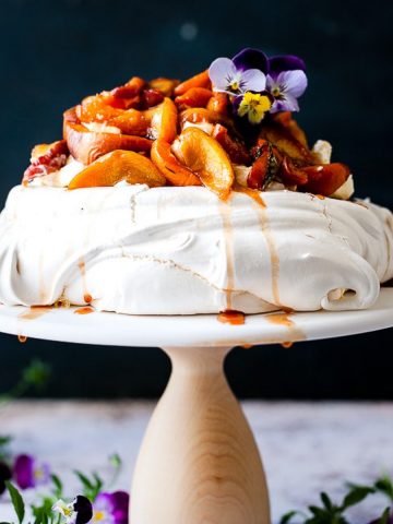 Pavlova with roasted fruit on a cake stand.