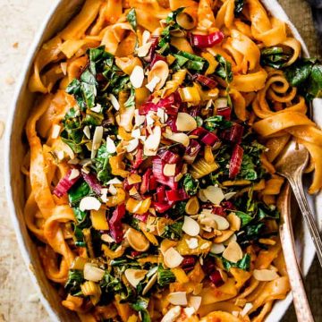 Roasted red pepper pasta with wilted greens in a white dish with a fork and spoon.