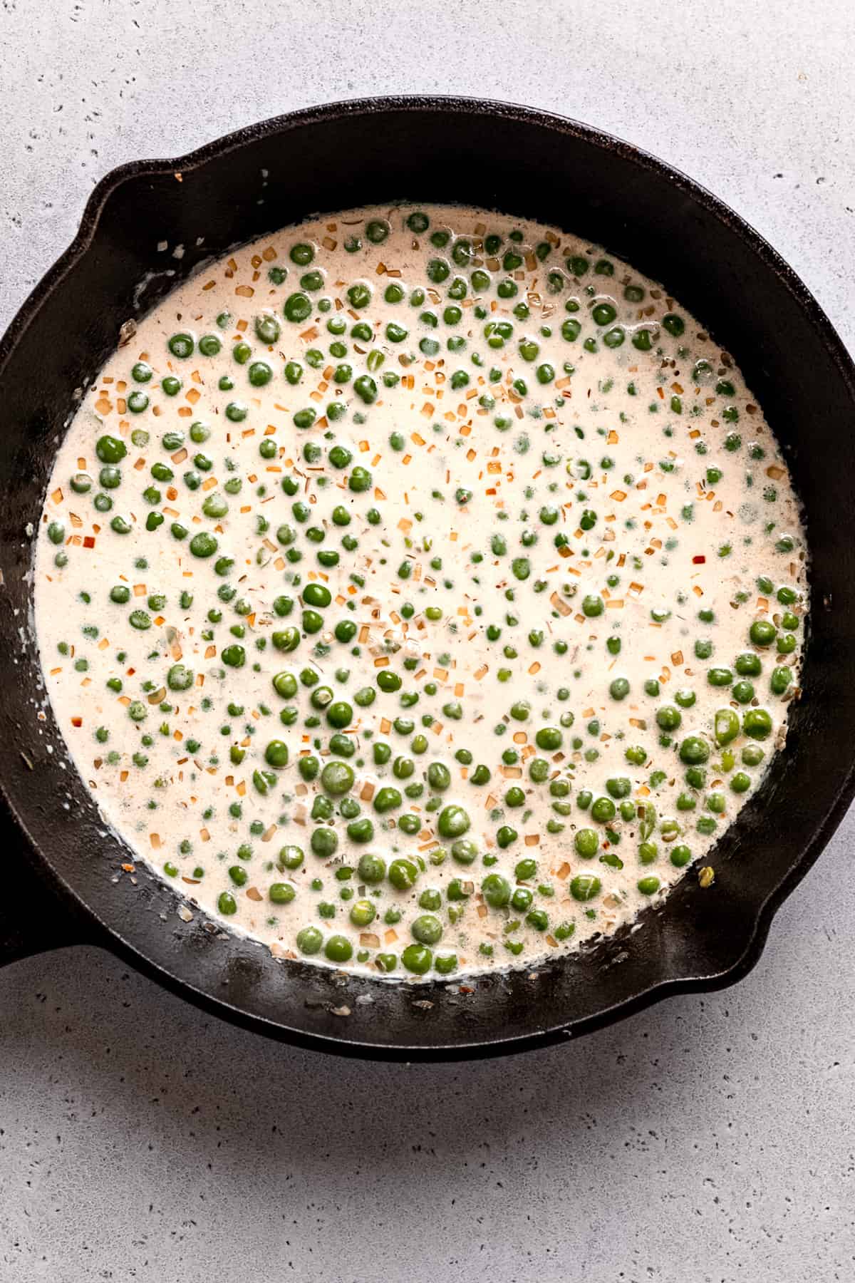Adding cream to the peas in a skillet.
