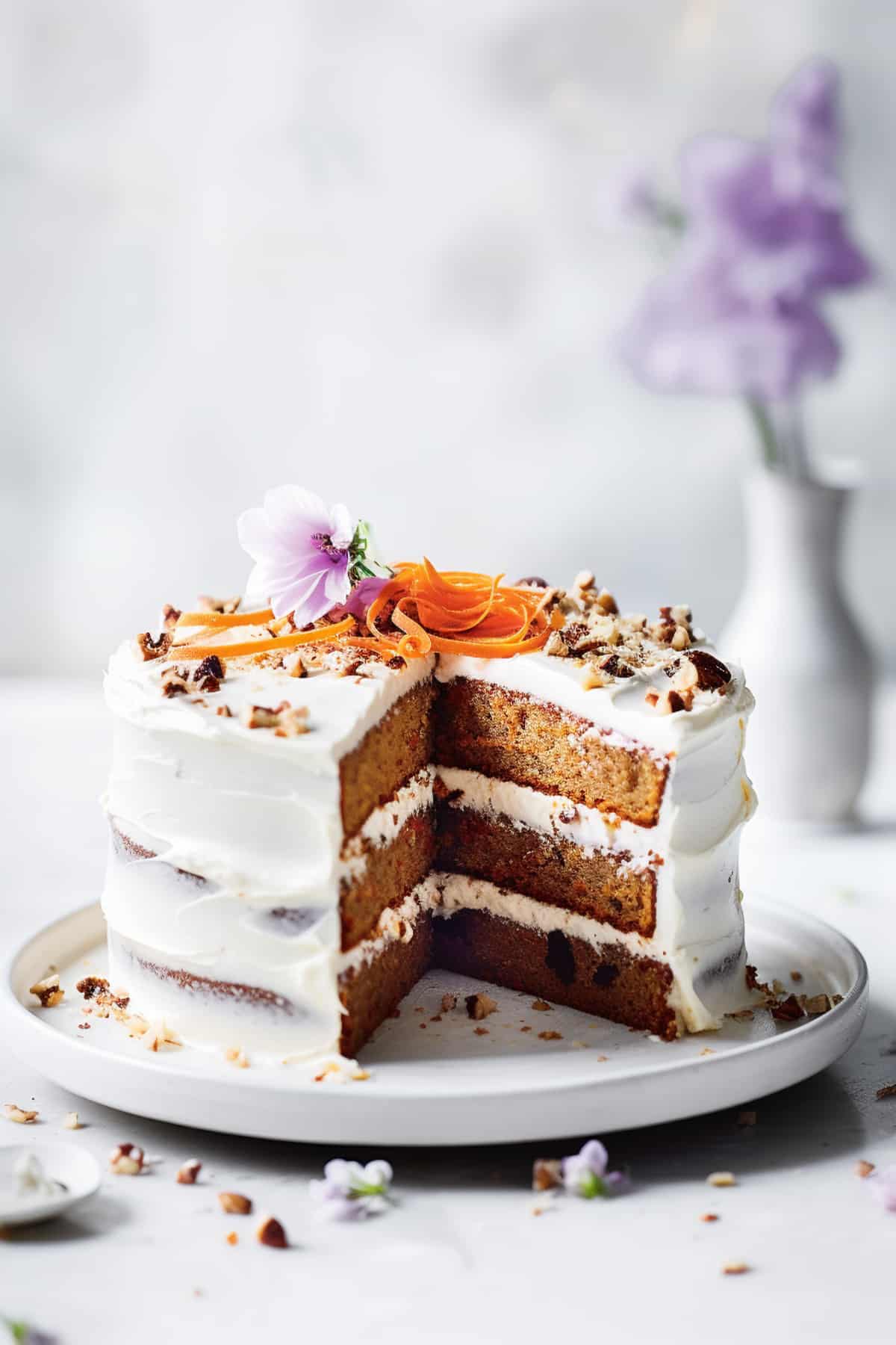 A carrot cake with cream cheese frosting on a white plate.