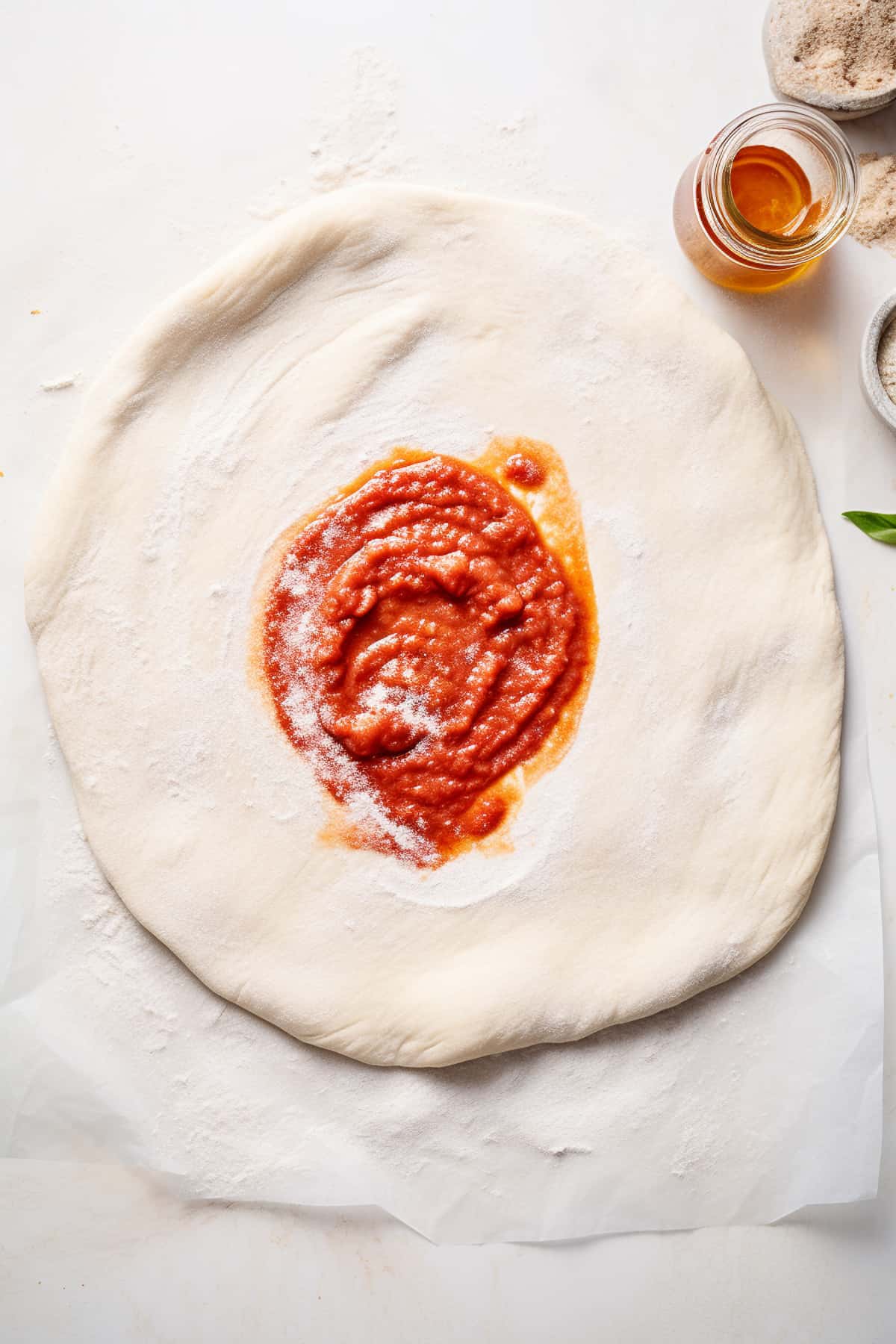 Pizza dough with sauce spread on it.
