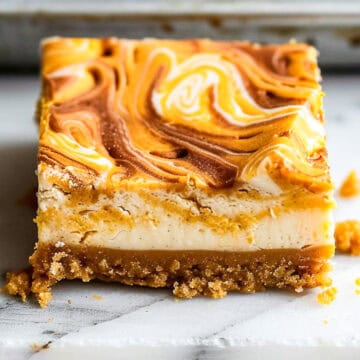 Pumpkin swirl cheesecake bars on a marble cutting board with nutmeg and cinnamon.