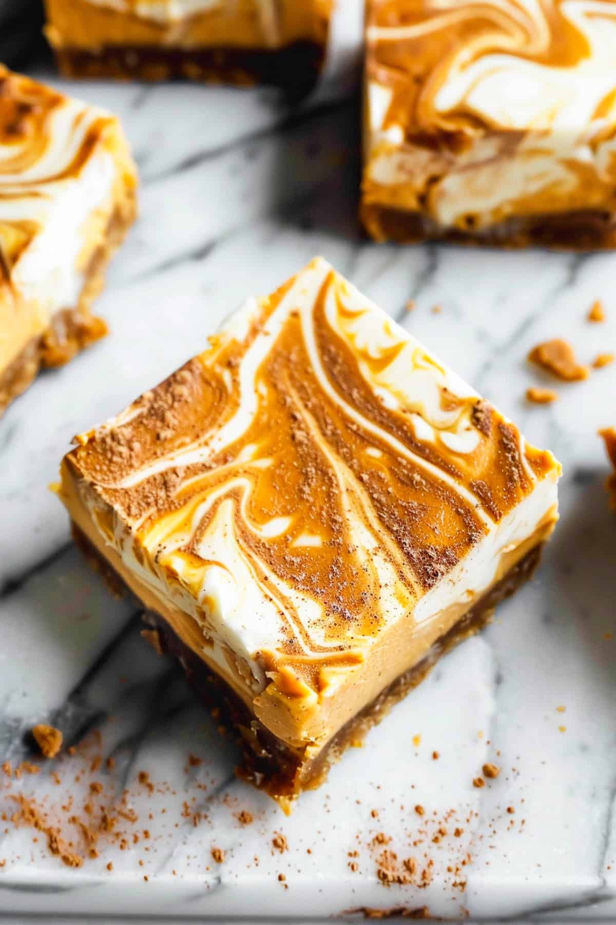 Pumpkin swirl cheesecake bars on a marble cutting board with nutmeg and cinnamon.