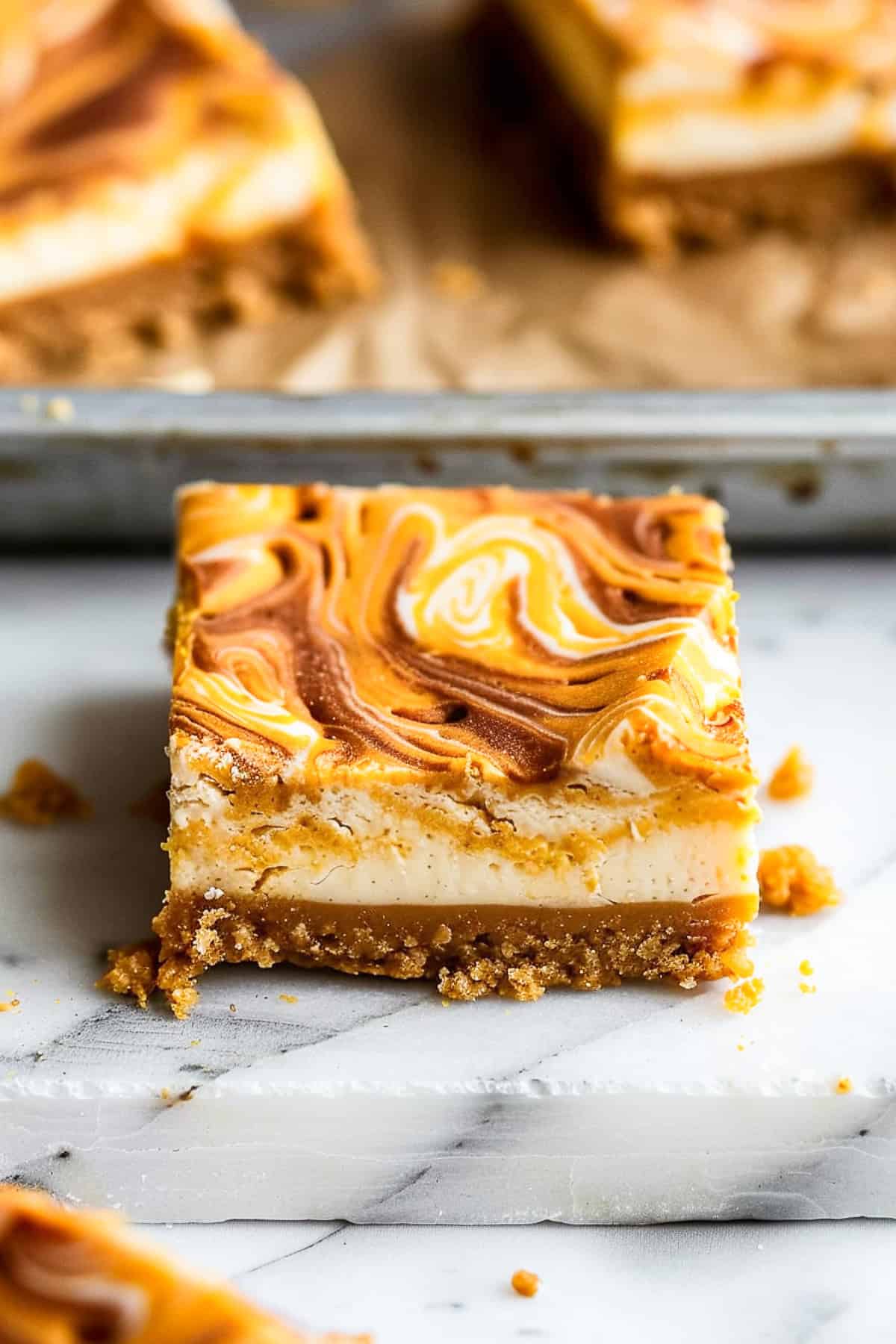 Pumpkin swirl cheesecake bars on a marble cutting board with nutmeg and cinnamon.