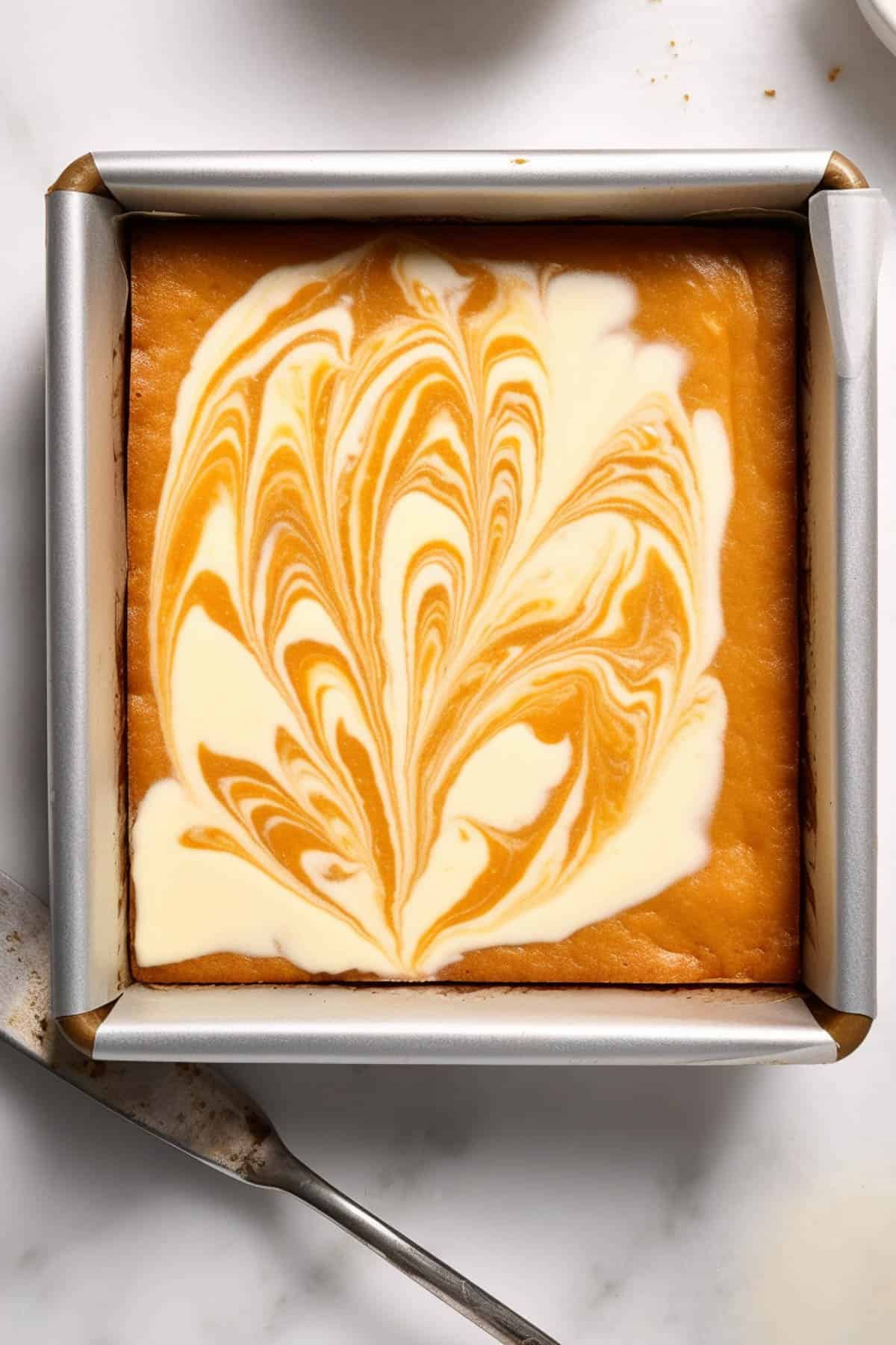 Pumpkin swirl cheesecake bars in a square tin before being cut.