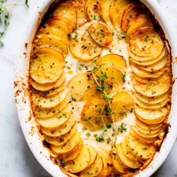 Potatoes au gratin with gruyere in a baking dish with fresh thyme.