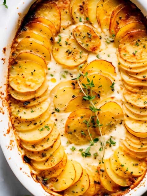 Potatoes au gratin with gruyere in a baking dish with fresh thyme.
