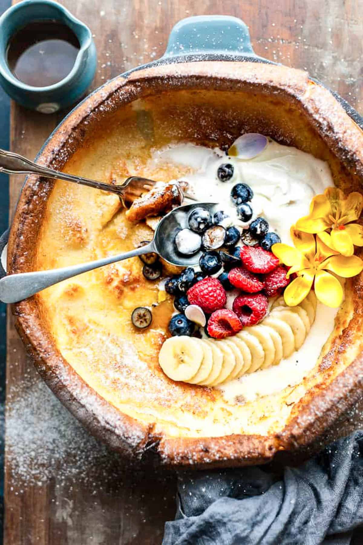 Dutch baby pancake with cream and maple syrup in a skillet.