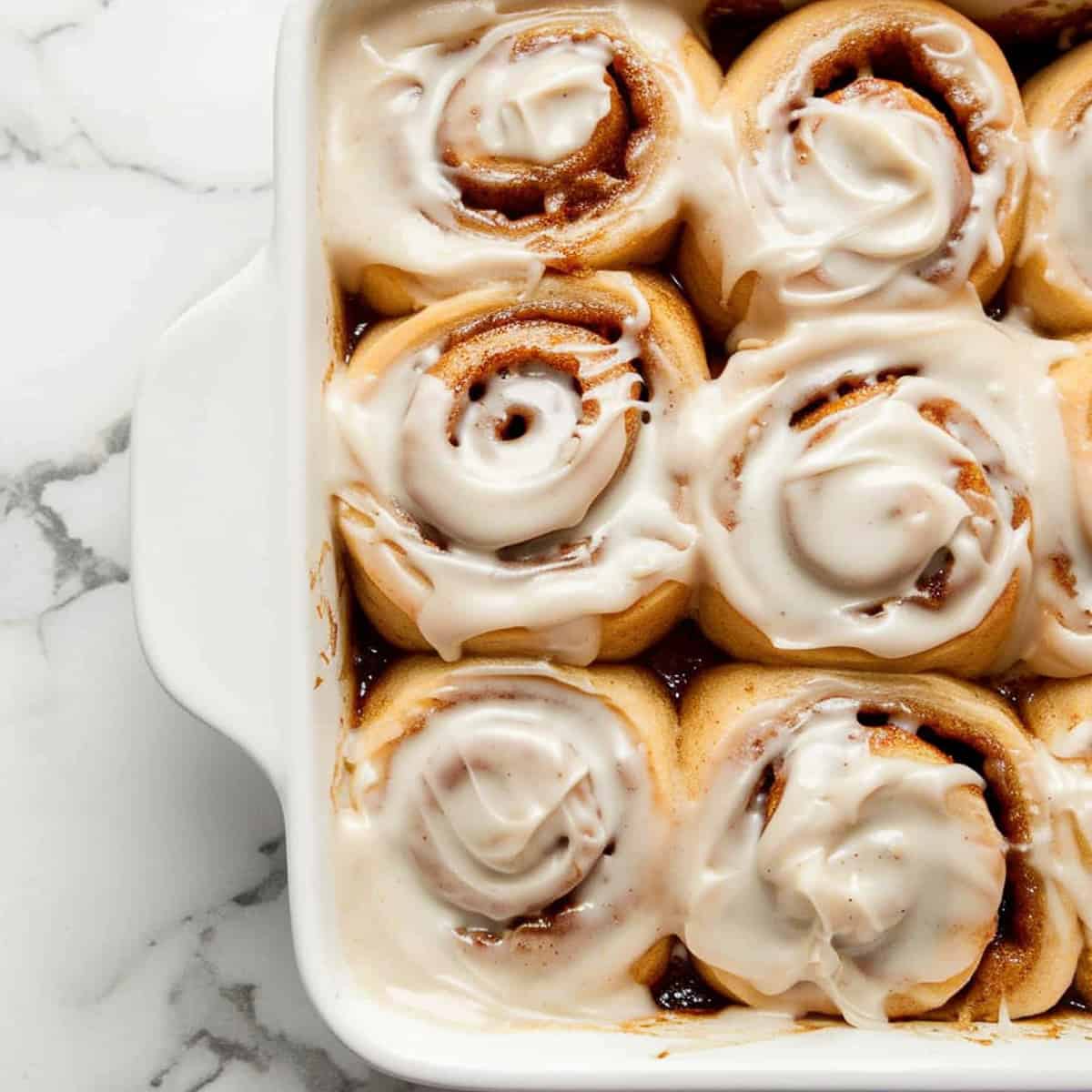 Apple pie cinnamon buns with cream cheese frosting in a ceramic dish.
