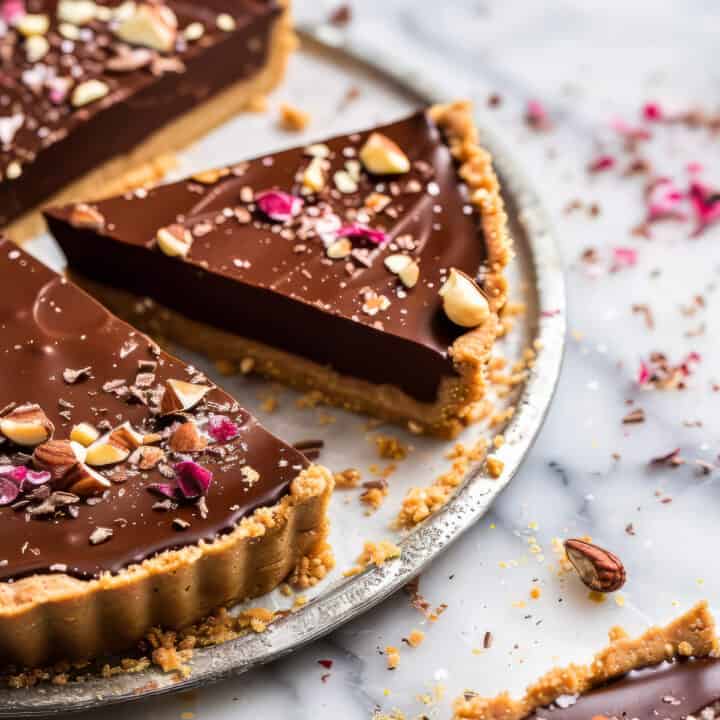 Chocolate hazelnut tart on a marble cake plate with chopped hazelnuts.