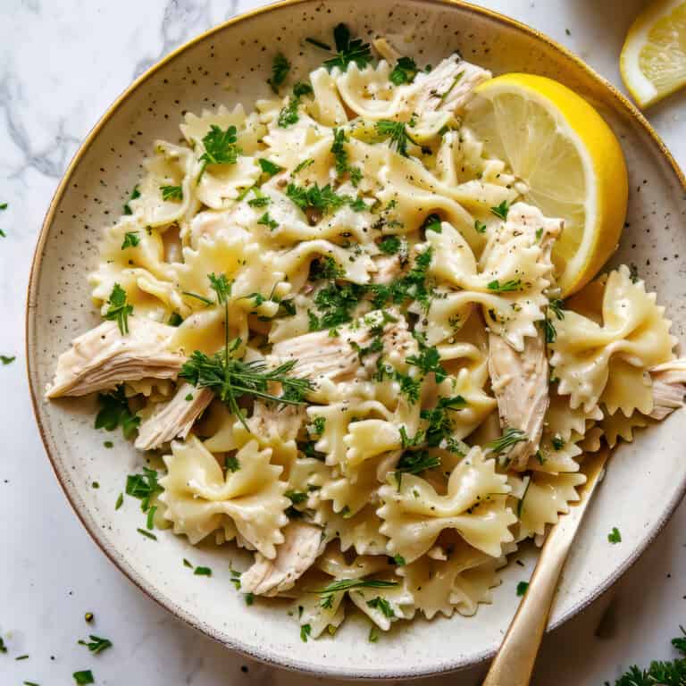 Easy Lemon Chicken Pasta Salad on a white bowl with herbs.