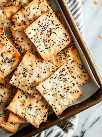 Homemade flatbread crackers with seeds on a baking tray.