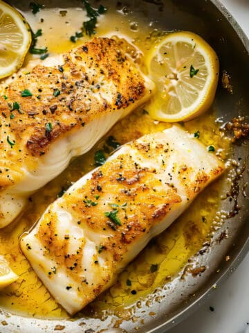 Pan fried cod with lemon butter sauce in a pan.