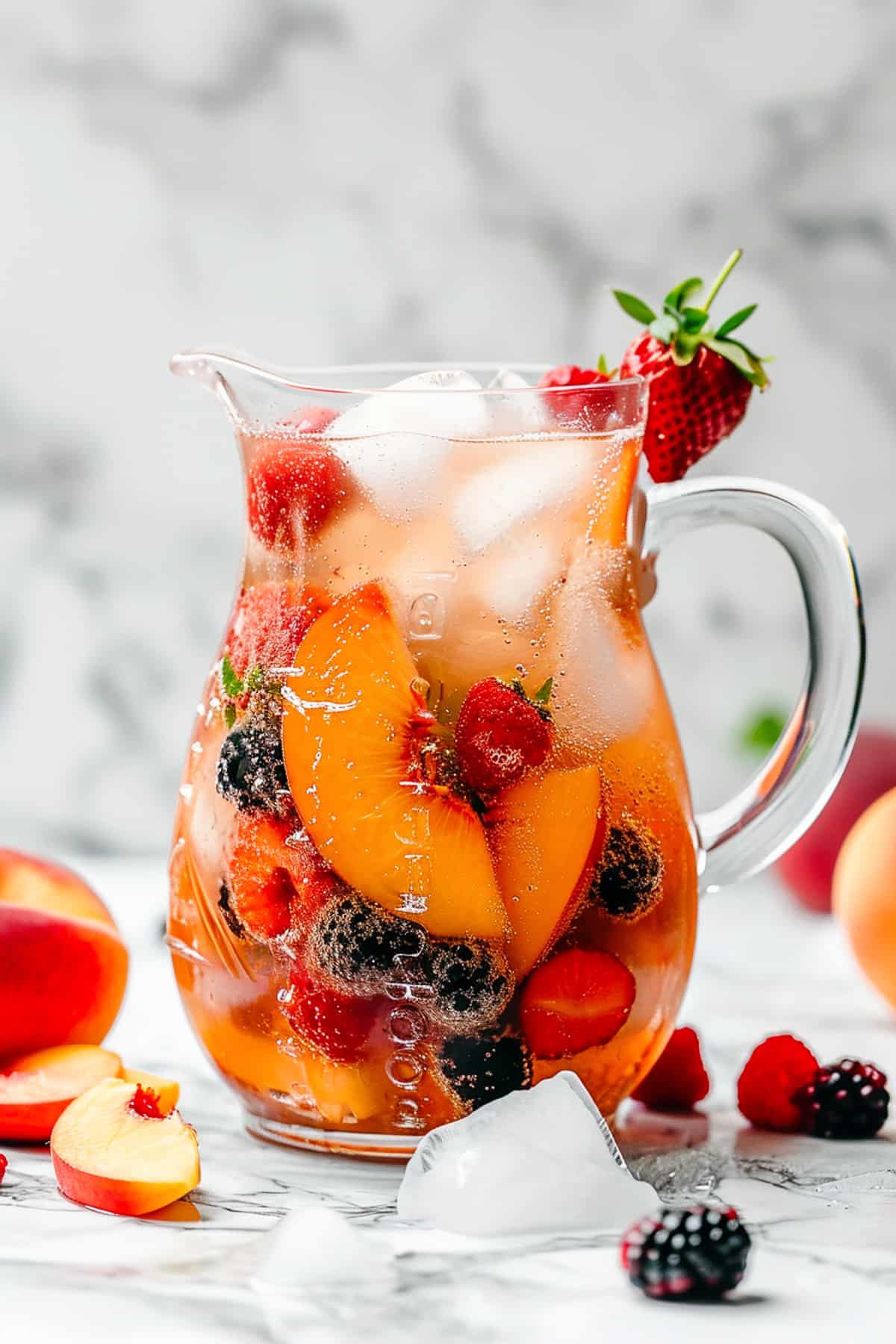 Peach sangria in a pitcher with peaches and berries.