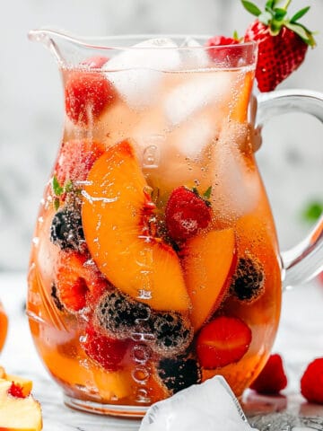 Peach sangria in a pitcher with peaches and berries.