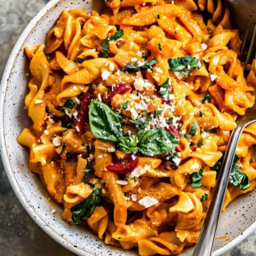 Roasted red pepper pasta with green and parmesan cheese in a bowl.