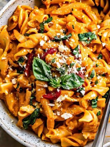 Roasted red pepper pasta with green and parmesan cheese in a bowl.