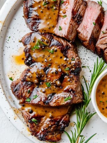 Seared sirloin steak with whisky peppercorn sauce on a white plate.