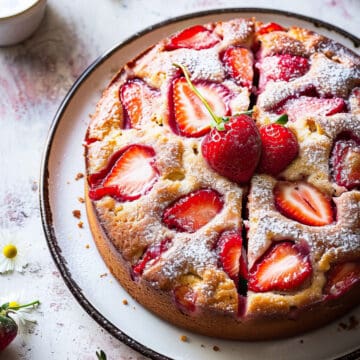 Easy strawberry cake on a white plate with icing sugar.