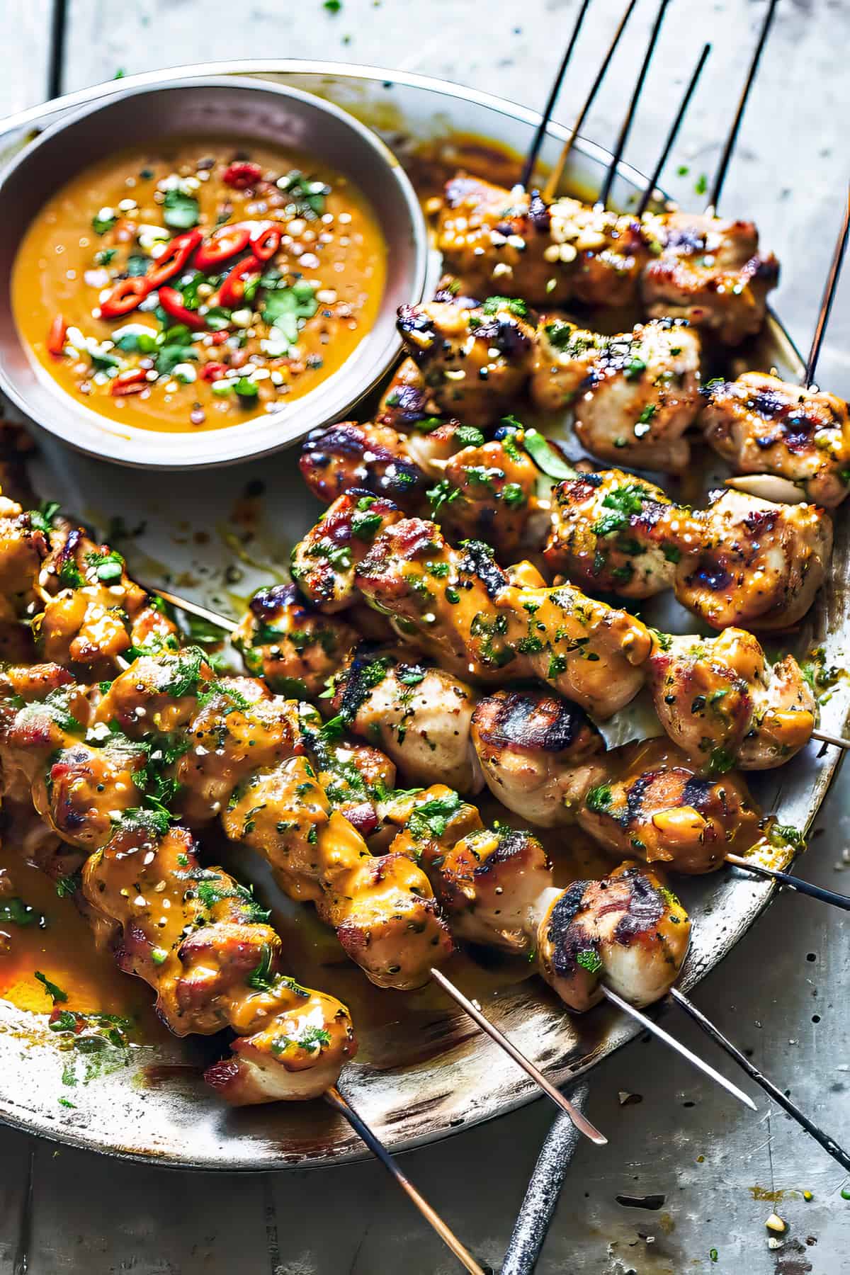 Thai grilled chicken skewers with peanut sauce and cilantro on a plate.