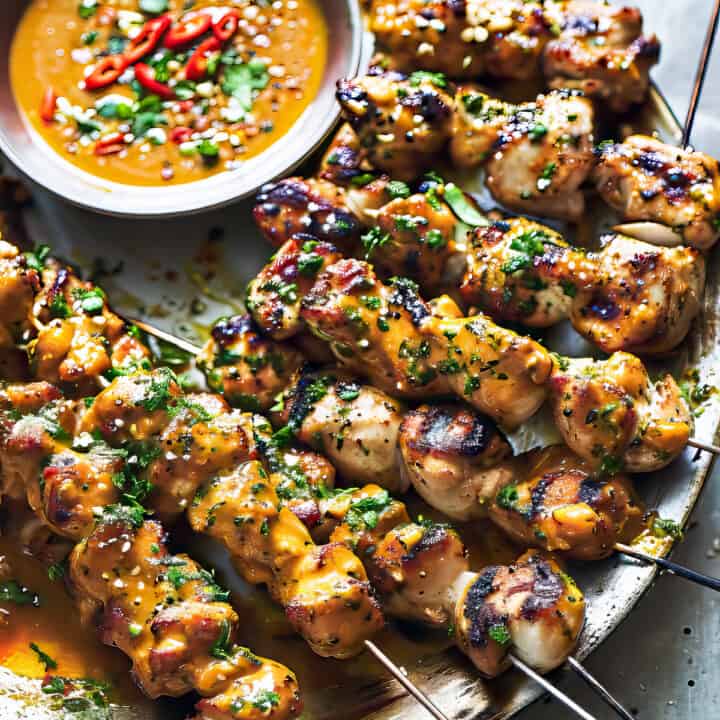 Thai grilled chicken skewers with peanut sauce and cilantro on a plate.