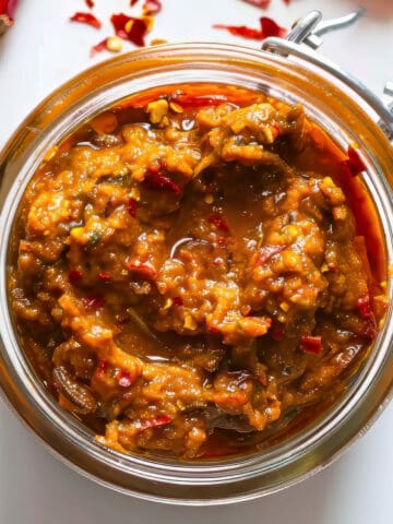 Homemade Thai red curry paste in a jar on a white table.