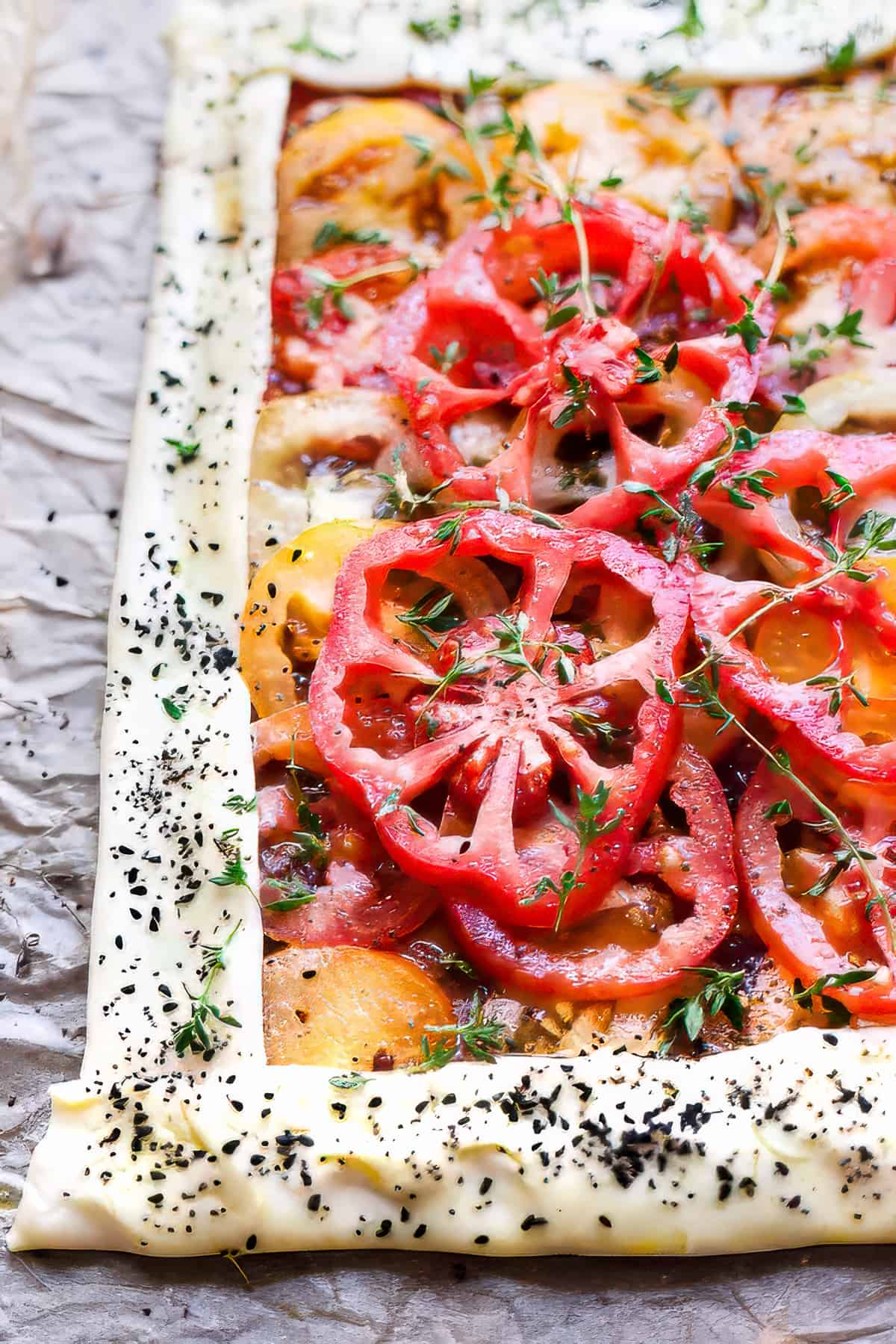 Unbaked tomato tart with thyme and basil on a baking tray.