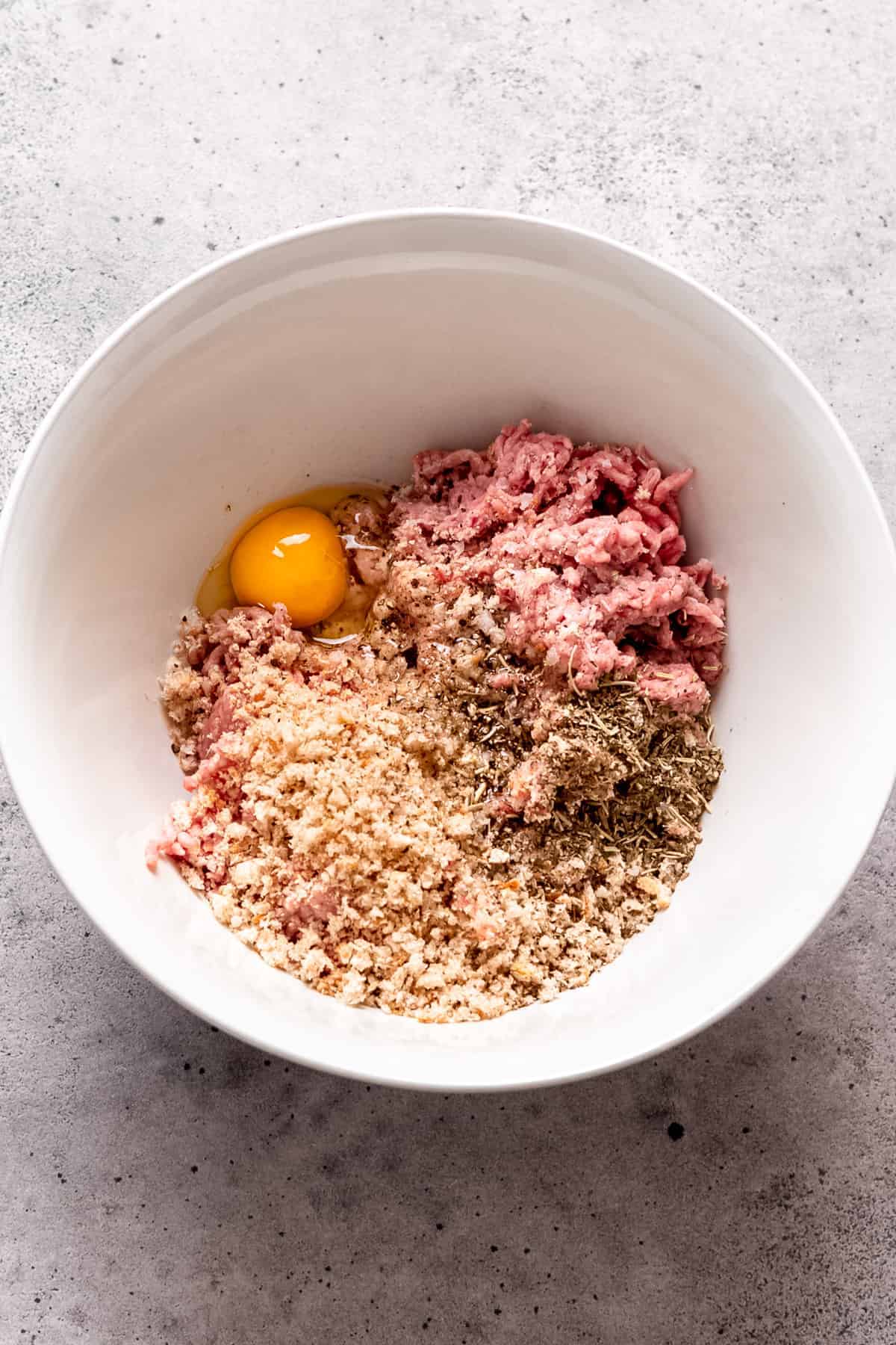Greek chicken meatball mixture in a bowl with breadcrumbs and egg.