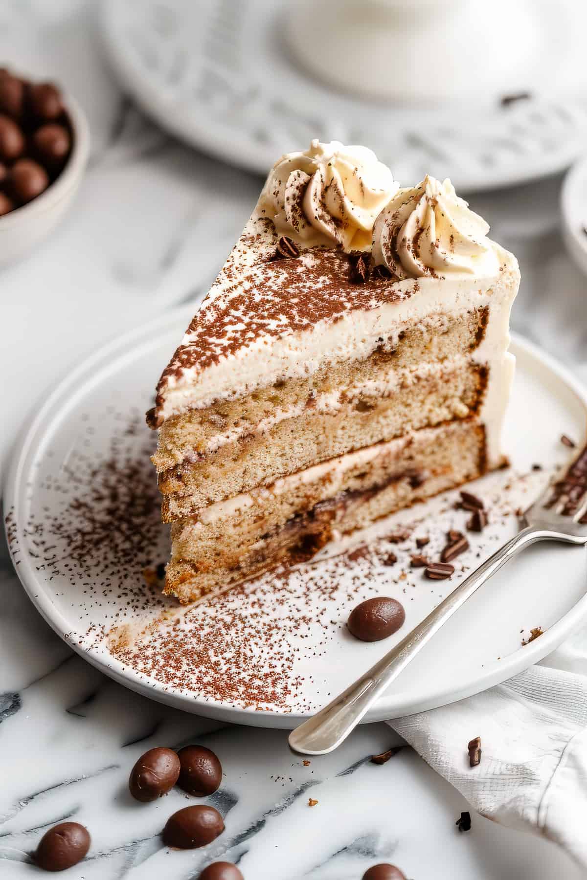 A slice of tiramisu layer cake with a fork and some coffee beans.