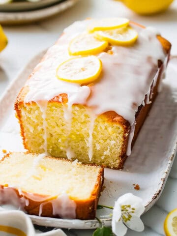 Fluffy lemon drizzle cake on a white plate with drizzle icing.