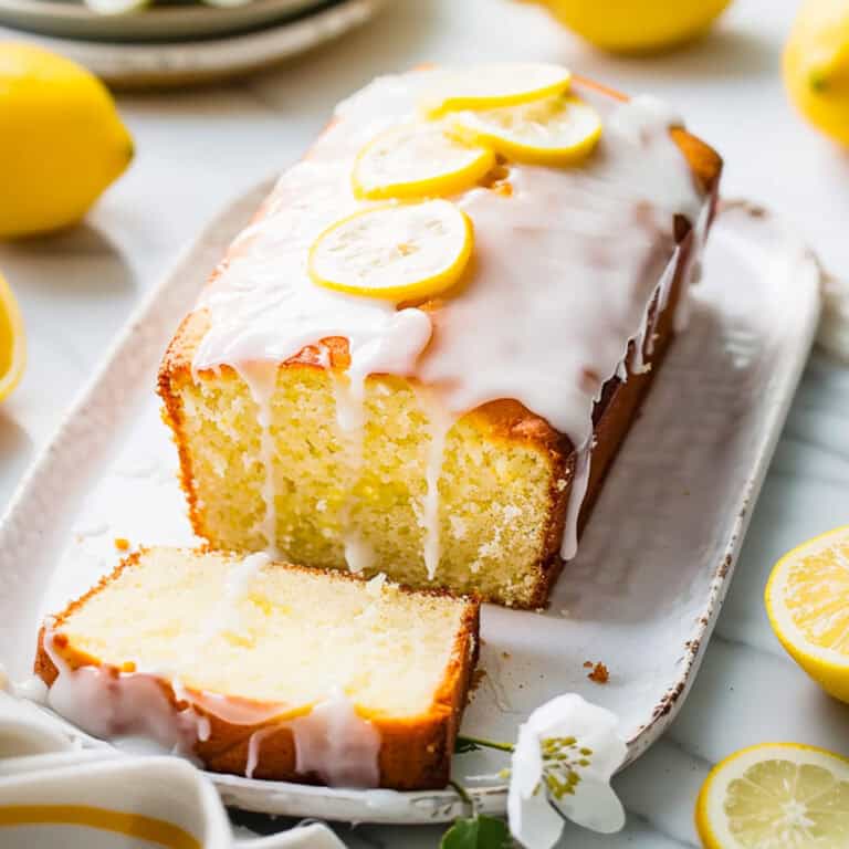 Fluffy lemon drizzle cake on a white plate with drizzle icing.
