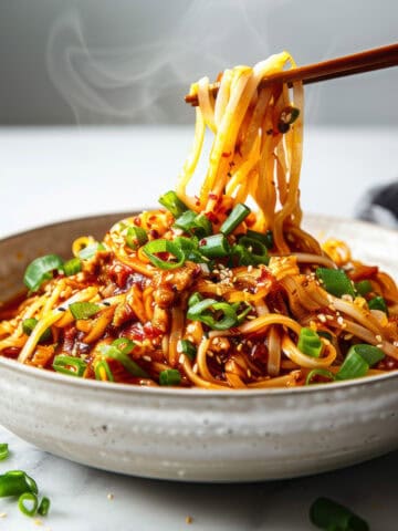 Easy szechuan noodles with green onions in a white bowl.