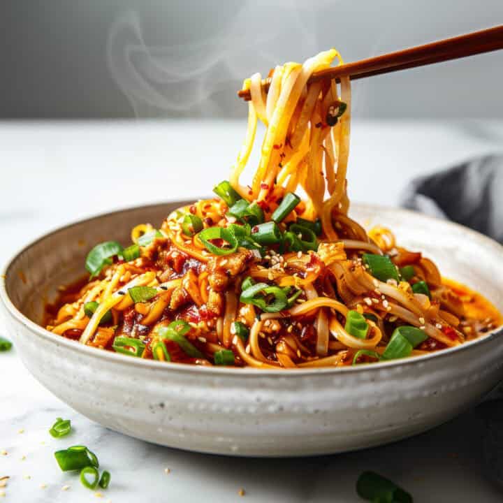 Easy szechuan noodles with green onions in a white bowl.