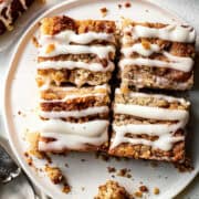 Apple coffee cake with cream cheese glaze on a white plate.